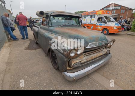 Rayleigh, Großbritannien. Mai 2023. Ein verwitterter Chevrolet Pickup-Truck mit Patina-Finish parkt auf einer Rayleigh-Straße während eines öffentlichen Treffens. Die Szene umfasst ein orange-weißes „Farm Fresh“-Schild, einen Eiswagen und bewundernde Zuschauer, die an Nostalgie und Gemeinschaftsgeist erinnern. Farm Fresh Garage Truck und amerikanische Fahrzeuge werden gezeigt. Penelope Barritt/Alamy Live News Stockfoto