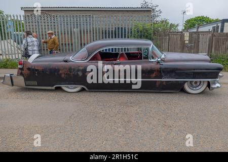Rayleigh, Großbritannien. Mai 2023. Ein verwitterter Custom Car im Stil der 1950er Jahre mit weißen Wänden und rotem Innenraum, der auf einer asphaltierten Straße in Rayleigh, Essex, parkt. Drei Personen stehen in der Nähe eines Zauns mit Industriegebäuden und Grünflächen im Hintergrund. Farm Fresh Garage Truck und amerikanische Fahrzeuge werden gezeigt. Penelope Barritt/Alamy Live News Stockfoto