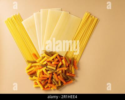 Nudeln. Verschiedene Arten roher Pasta auf beigefarbenem Hintergrund. Kreative Komposition mit Lasagne, Spaghetti und Fusilli. Italienisches Speisekonzept Stockfoto