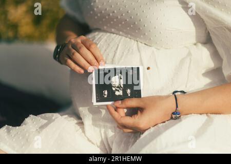 Nahaufnahme des Bauches einer schwangeren Frau, während sie das Ultraschallbild ihres Babys hält. Stockfoto