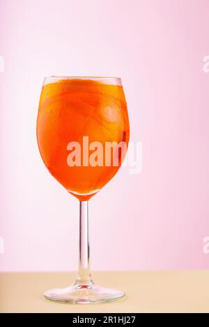 Ein Glas Aperol Spritz Cocktail auf pinkfarbenem Beige Hintergrund. Cocktail Aperol Spritz mit Orange und Eiswürfeln. Sommerliche Erfrischungsgetränke Stockfoto