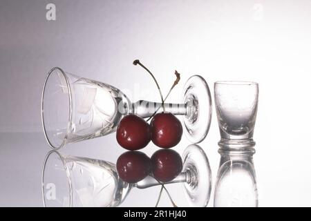 Vintage-Gläser aus fein bearbeitetem Glas aus dem Ende des 19. Jahrhunderts, italienische Kirschen auf weißem Hintergrund und zwei Kirschen im Vordergrund Stockfoto