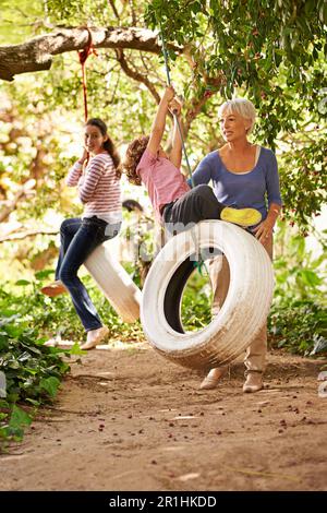 Großmutter, Garten und Enkel spielen mit Seniorin auf Reifenschaukel oder im Urlaub und haben Spaß im Sommer. Aufgeregt, Enkelkinder und draußen Stockfoto