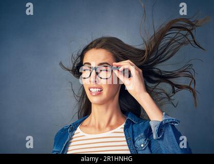Es wird ziemlich windig hier drin. Eine glückliche junge Frau, die im Studio Luft ins Gesicht geblasen hat. Stockfoto