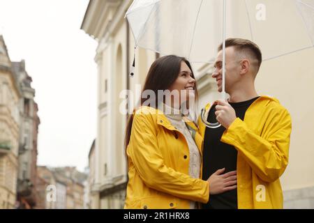 Reizendes junges Paar mit Regenschirm, das unter Regen auf der Straße der Stadt spaziert Stockfoto