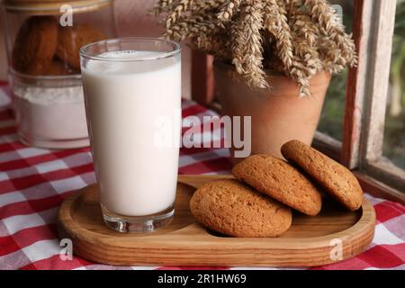 Glas Milch mit Keksen auf roter karierter Tischdecke im Innenbereich Stockfoto