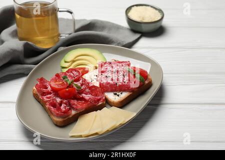 Leckere Toasts mit Wurstscheiben, Tomaten und Käse auf einem weißen Holztisch Stockfoto
