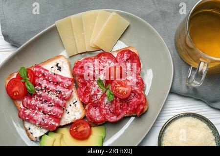 Leckere Toasts mit Wurstscheiben, Tomaten und Käse auf einem weißen Holztisch, flach liegend Stockfoto