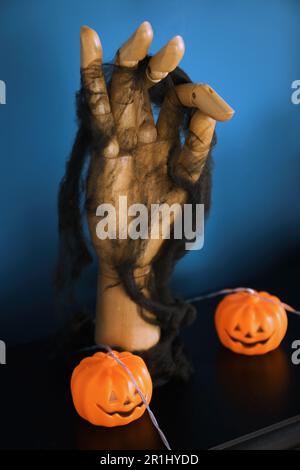 Jack-o'-Laternen-Lampen und Holzhand auf einem schwarzen Kamintisch in der Nähe der blauen Wand Stockfoto