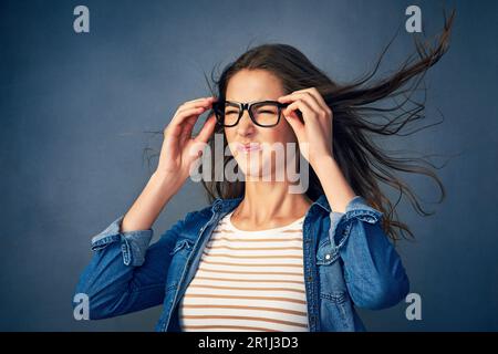 Kann jemand den Ventilator abstellen? Eine glückliche junge Frau, die im Studio Luft ins Gesicht geblasen hat. Stockfoto