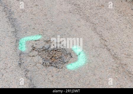 Grüne sprühlackierte Markierungen auf dem Asphalt auf einer kleinen Straße. Für Straßenreparaturen in Großbritannien, Wartungskonzept, verschleißarme Metapher. Stockfoto