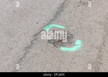 Grüne sprühlackierte Markierungen auf dem Asphalt auf einer kleinen Straße. Für Straßenreparaturen in Großbritannien, Wartungskonzept, verschleißarme Metapher. Stockfoto