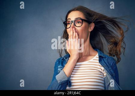 Sie ist von dem, was sie gerade gehört hat, umgehauen. Eine glückliche junge Frau, die im Studio Luft ins Gesicht geblasen hat. Stockfoto