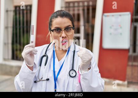 Junge hispanische Ärztin, die eine Coronavirus-Infektion macht Nasentest ahnungslos und verwirrter Ausdruck. Zweifelhaftes Konzept. Stockfoto