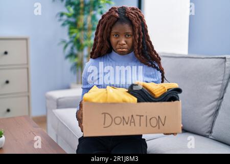 Afrikanische Frau, die Spendenboxen für wohltätige Zwecke hält, deprimiert und besorgt wegen Not, weinend wütend und verängstigt. Trauriger Ausdruck. Stockfoto