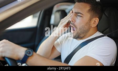 Ein junger hispano-Mann, der müde ist, ein Auto zu fahren, das auf der Straße gähnt Stockfoto