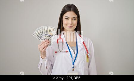 Junge, wunderschöne hispanische Ärztin, die selbstbewusst Dollar hält, vor isoliertem weißem Hintergrund Stockfoto