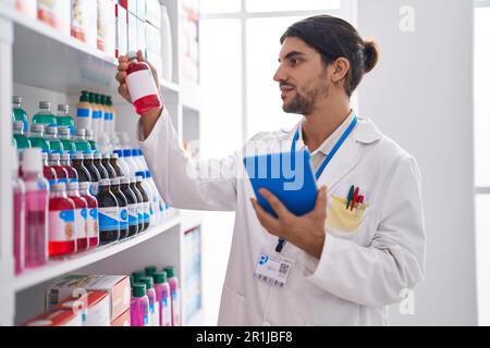 Junger hispanic-Mann Apotheker mit Touchpad hält Medikamentenflasche in der Apotheke Stockfoto