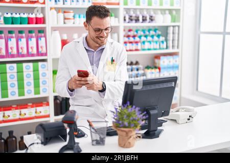 Junger hispanic-Mann Apotheker im Gespräch auf Smartphone mit Computer in der Apotheke Stockfoto