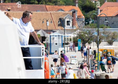 Insel Zlarin, Kroatien - 22. Juli 2022: Menschen verlassen den Pier und ein Mann, der auf einer Jadrolinija-Fähre arbeitet und vom Deck aus beobachtet Stockfoto