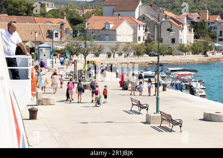 Insel Zlarin, Kroatien - 22. Juli 2022: Menschen verlassen den Pier und ein Mann, der auf einer Jadrolinija-Fähre arbeitet und vom Deck aus beobachtet Stockfoto