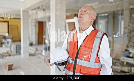 Leitender, grauhaariger Architekt, gestresst mit Schutzhelm auf der Baustelle Stockfoto