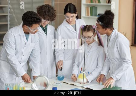 Eine vielfältige Gruppe junger Teenager, die Labormäntel tragen und wissenschaftliche Experimente in der Schule mit der Hilfe eines Lehrers durchführen Stockfoto