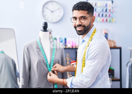 Ein junger arabischer Schneider, der eine selbstbewusste Messjacke im Schneiderladen lächelt Stockfoto
