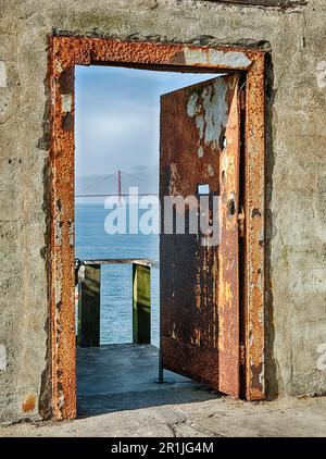 Eine rostige Tür im Gefängnishof des Alcatraz Penitentiary öffnet sich zu einem Blick auf die San Francisco Bay und die Golden Gate Bridge. Stockfoto