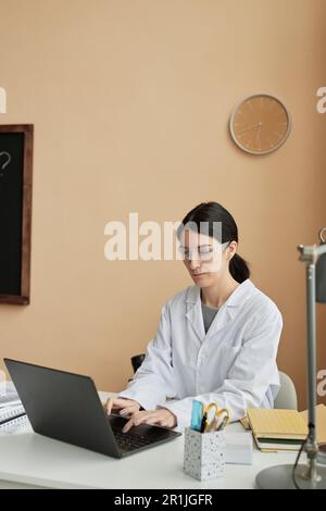 Vertikales Porträt einer Lehrerin für Naturwissenschaften, die im Klassenzimmer ein Notebook benutzt, kopieren Sie oben Stockfoto