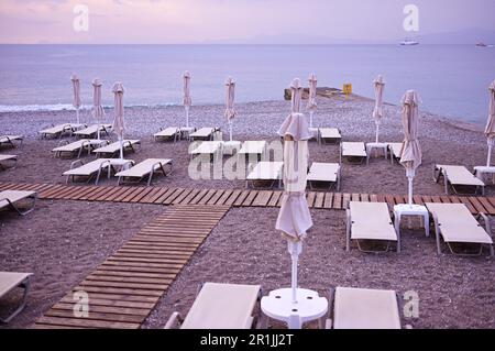 Die Küste der Insel und ein gut ausgestatteter Strand für Touristen mit Sonnenliegen und Sonnenschirmen in einer Reihe und Holzdecks zwischen den Sonnenliegen. Stockfoto