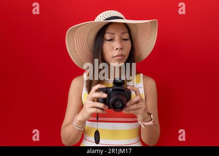 mittelalterliche chinesin, die eine Reflexkamera benutzt und einen Sommerhut trägt, ahnungslos und verwirrter Gesichtsausdruck. Zweifelhaftes Konzept. Stockfoto