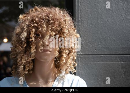 Eine weibliche Plastikpuppe mit geschwungener Perücke steht vor der Fassade eines Modegeschäfts Stockfoto