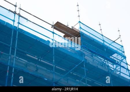 Gerüste mit Schutznetz gegen ein Gebäude, um zu verhindern, dass Farbe und Baumaterial während der Renovierung auf die Straße und Menschen fallen Stockfoto