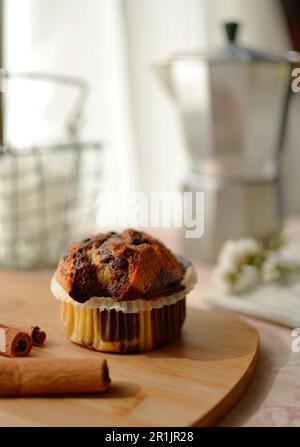 Vanille-Schokoladenkuchen in einer Wellform. Es gibt Zimtstangen auf dem Tisch, eine silberne Kaffeemaschine und einen Korb mit Zucker. Stockfoto