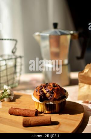 Vanille-Schokoladenkuchen in einer Wellform. Es gibt Zimtstangen auf dem Tisch, eine silberne Kaffeemaschine und einen Korb mit Zucker. Stockfoto