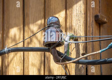 Porzellanisolator mit elektrischen Drähten an der Holzwand der Hütte. Garten, ländlich, Hütte. Stockfoto