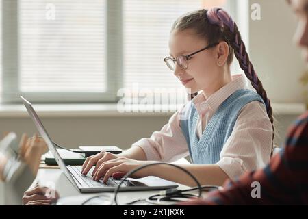 Seitliches Porträt eines lächelnden süßen Schulmädchens, das im Programmierkurs ein Notebook für Kinder verwendet Stockfoto