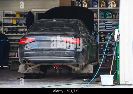 Schwarzes Auto ohne Räder in der Garage während der Aufhängungsreparatur und des Reifenwechsels aufgebockt Stockfoto