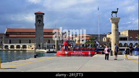 Hirschstatuen am Eingang zum alten Hafen von Rhodos. Im Hintergrund befindet sich eine gotische Kirche mit einem Glockenturm und einem roten U-Boot im Hafen. Stockfoto