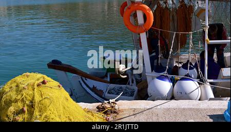 Ein Fischerboot mit Baldachin und Ausrüstung ist im Seehafen verankert. Am Ufer sind gelbe Fischernetze. Stockfoto