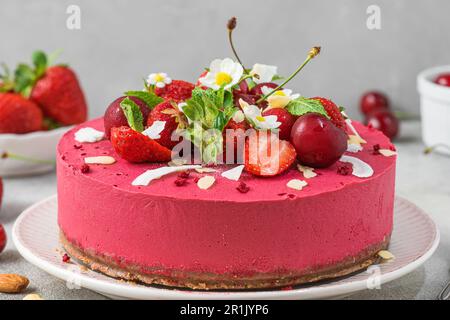 Roher veganer Erdbeeren- und Kirschkashewkuchen mit frischen Beeren, Nüssen und Blumen. Vegetarisches Dessert Stockfoto