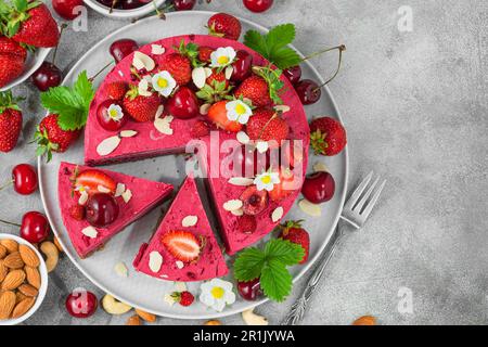 Roher, veganer Erdbeeren- und Kirschkashewkuchen mit frischen Beeren, Nüssen und Blumen. Vegetarisches Dessert. Draufsicht Stockfoto