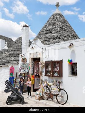 Kinder spielen Spielzeugflöten vor einem kleinen Laden in Rione Monti, Alberobello, Apulien Stockfoto