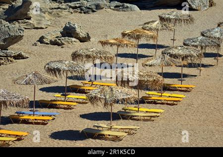 Sandstrand mit Sonnenliegen und Sonnenschirmen am Meer, auf der Insel. Die Liegen sind gelb und blau. Strohschirme neben den Sonnenliegen Stockfoto