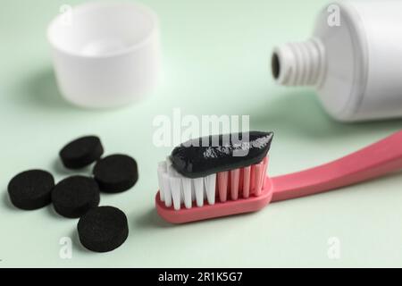 Bürste mit dunkelkohlensäurehaltiger Zahnpasta und Tabletten auf weißem Hintergrund, Nahaufnahme Stockfoto