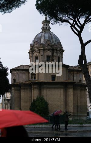 Die Kirche Santi Luca e Martina an einem regnerischen Tag mit Fußgängern mit Sonnenschirmen im Vordergrund Stockfoto