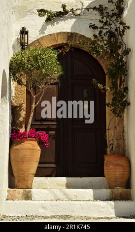 Eingangstüren der Häuser des Kapitäns in Lindos auf der Insel Rhodos. Weiße Wände, Holzbogentüren und Blumen am Eingang. Stockfoto