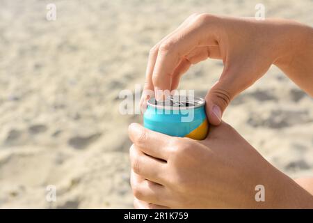 Frau öffnet Aluminiumdose mit Getränk auf Sand, Nahaufnahme. Platz für Text Stockfoto