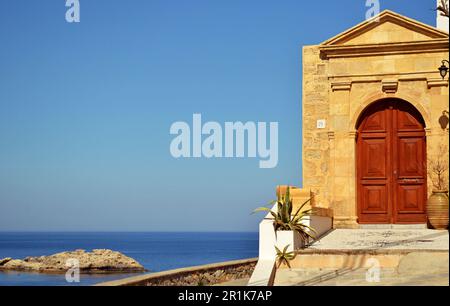 Mittelalterliche Bogentür aus Holz zu einem traditionellen Haus im griechischen Dorf Lindos. Steinbogen um die Tür und das Meer am Horizont Stockfoto